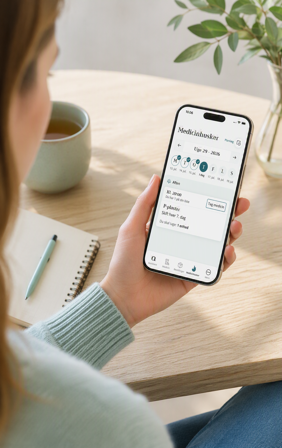 Kvinden sidder ved et bord og ser på Medicinhuskeren i apotekets app